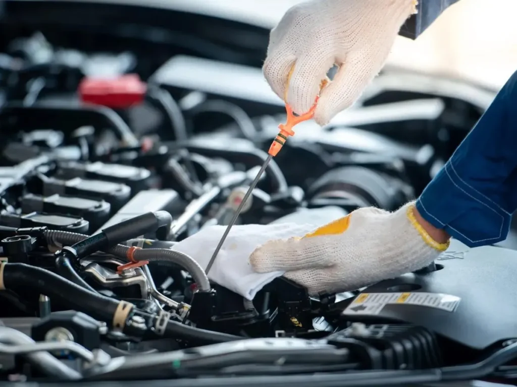 A mechanic wearing work gloves checks the oil dipstick in a car engine