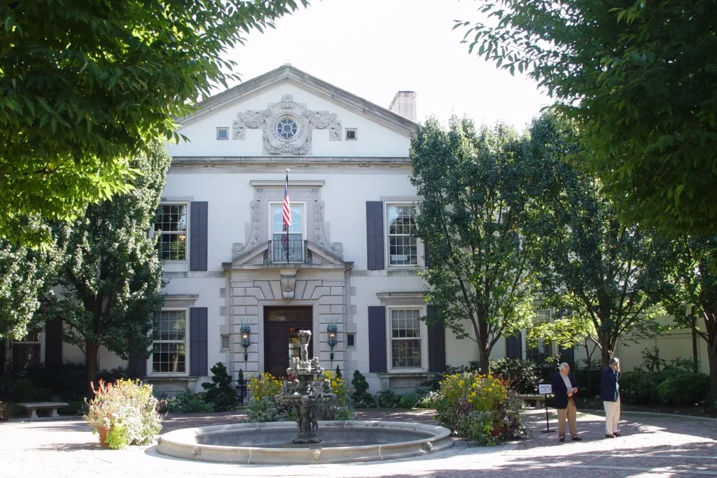 The Italian Renaissance style Alger House, home of the Grosse Pointe War Memorial, with a stone fountain in its front courtyard framed by trees on a sunny day