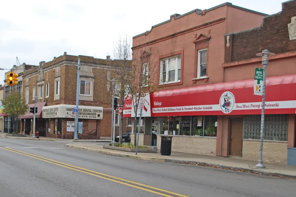 Two-story brick commercial buildings with awnings and storefronts along Joseph Campau Avenue at Norwalk Street in Hamtramck