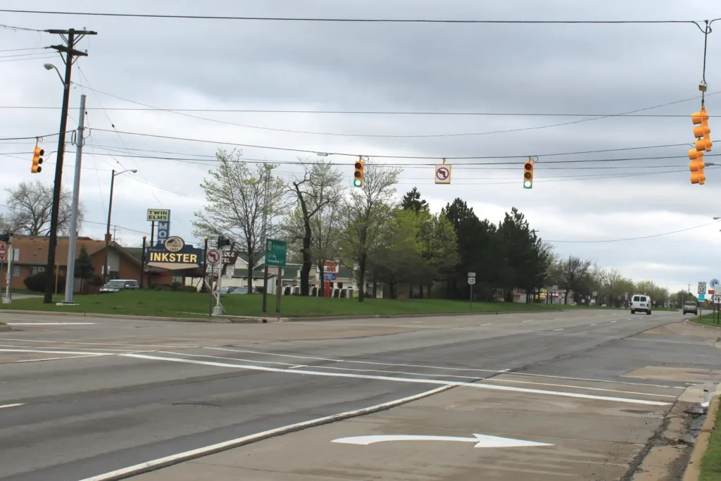 Wide view of Michigan Avenue (US-12) at Beech Daly Road in Inkster, with overhead traffic signals, an Inkster sign and low commercial buildings along the corridor