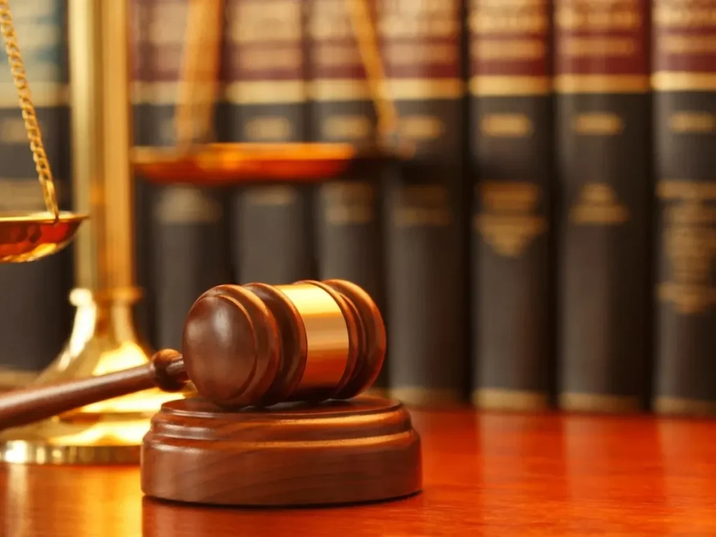 A wooden gavel and brass scales of justice in front of a row of law books