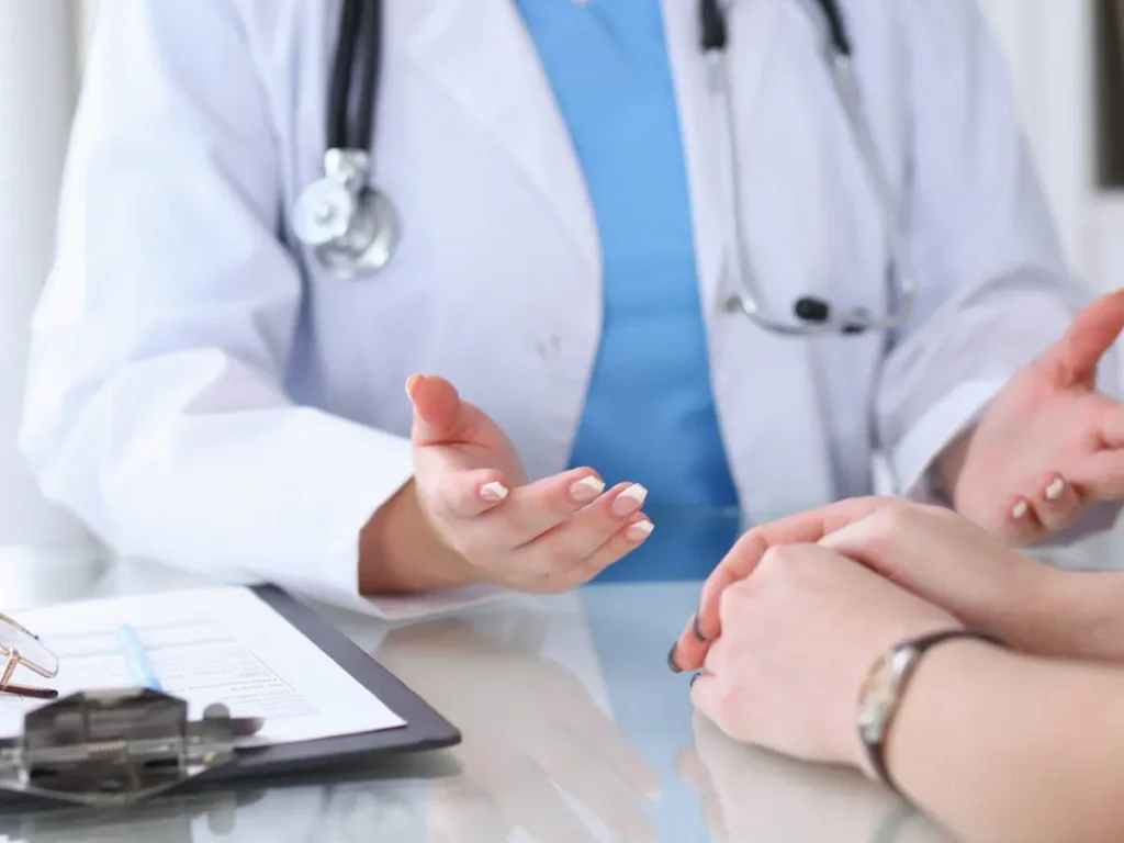 A doctor in a white coat with a stethoscope talks with a patient across a desk