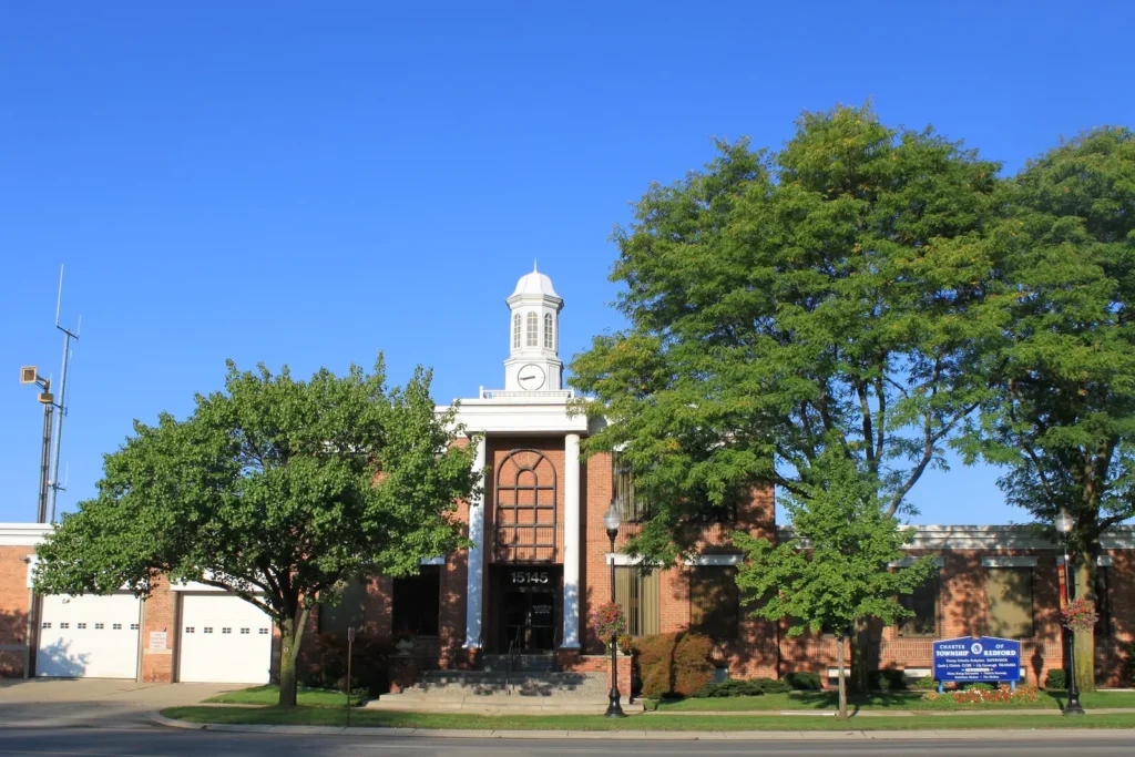 Redford Township Hall, a red brick building with white columns and a white clock cupola, on Beech Daly Road under a clear blue sky