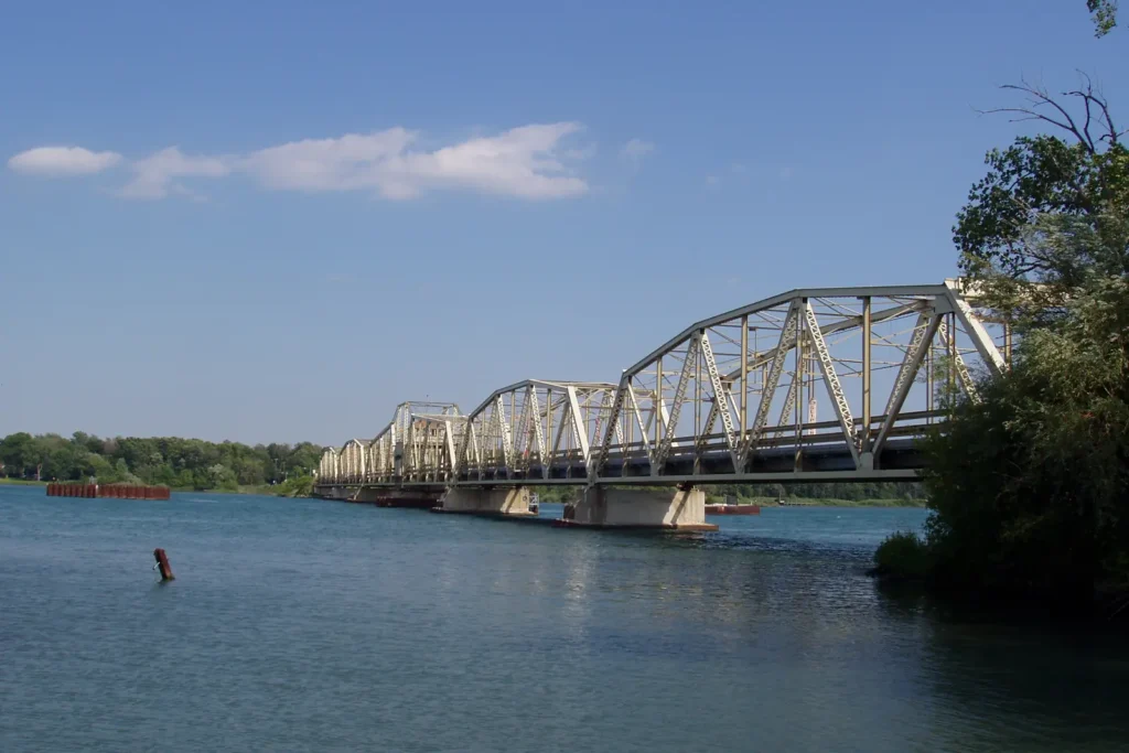 The steel truss Grosse Ile Toll Bridge crossing the Trenton Channel of the Detroit River, seen from the Riverview boat launch on a sunny day